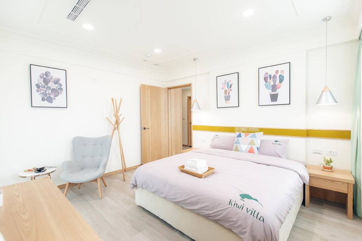 A modern hotel room with a bed, a chair, a small table, and artwork on the walls.