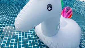 A white unicorn inflatable float in a pool with blue tiles and a clear sky. - Kiwi Villa (Magong)