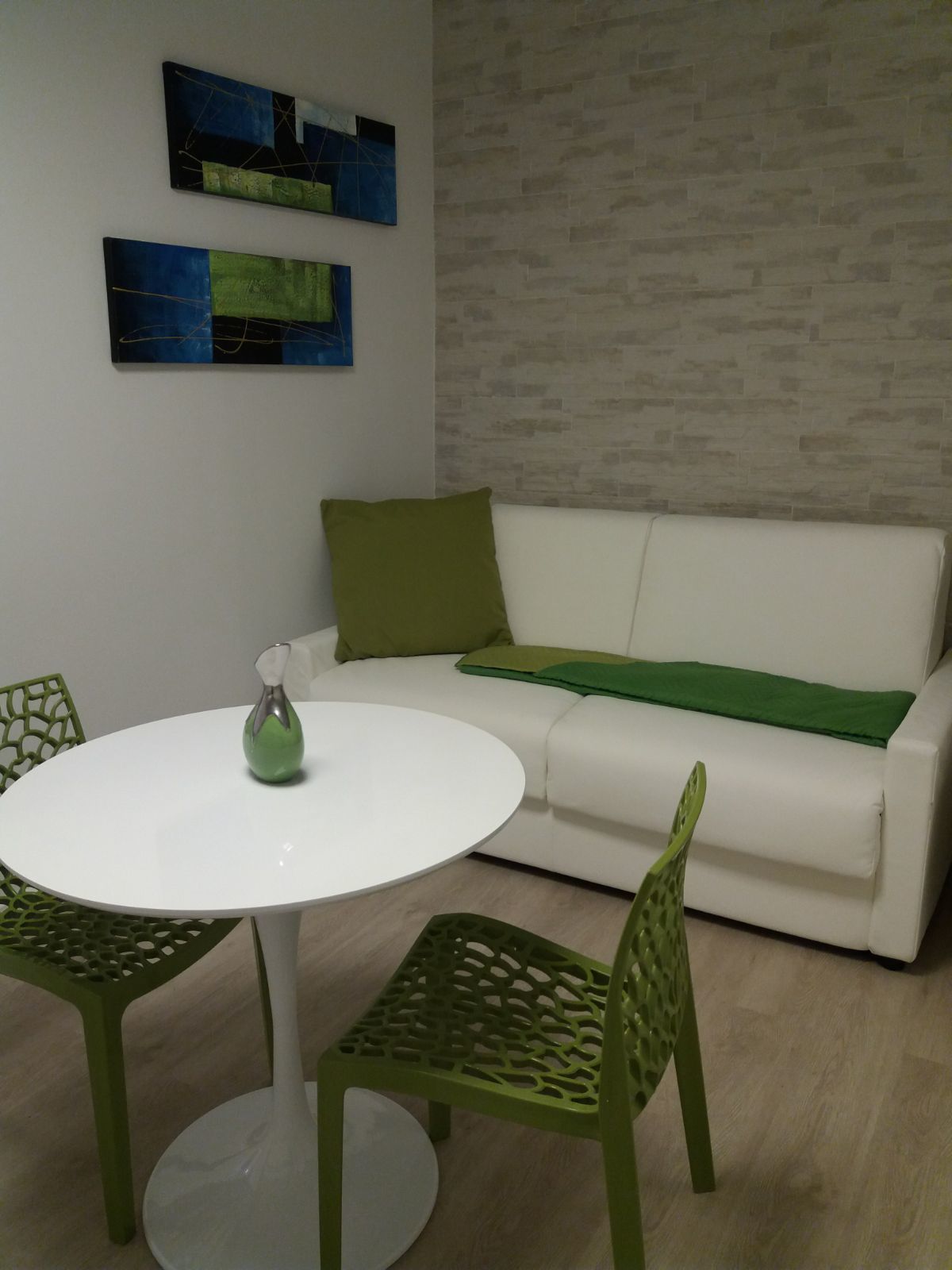 Un salon moderne avec un canapé blanc, des coussins verts, une table ronde blanche et des chaises vertes. Des tableaux abstraits ornent le mur.