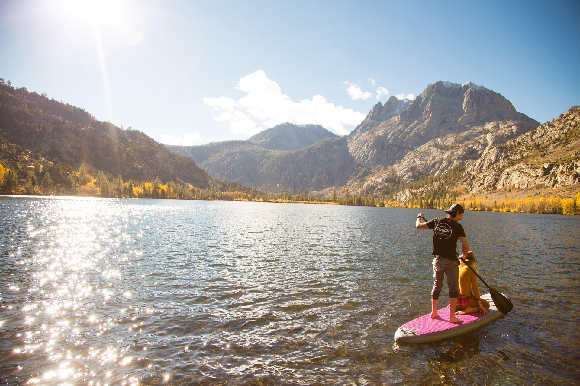 A person paddleboarding on a calm lake with mountains in the background.
