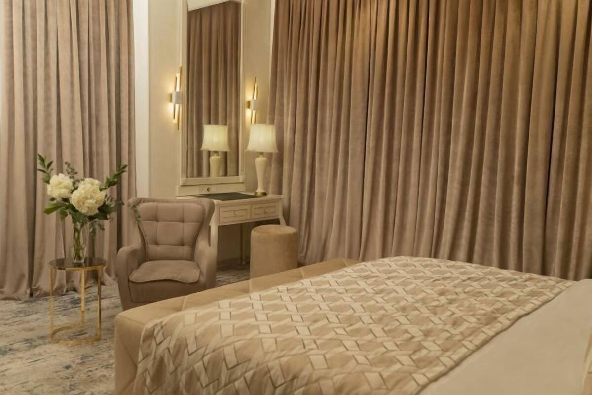 A hotel room with a bed, a chair, a vanity with a mirror, and curtains.