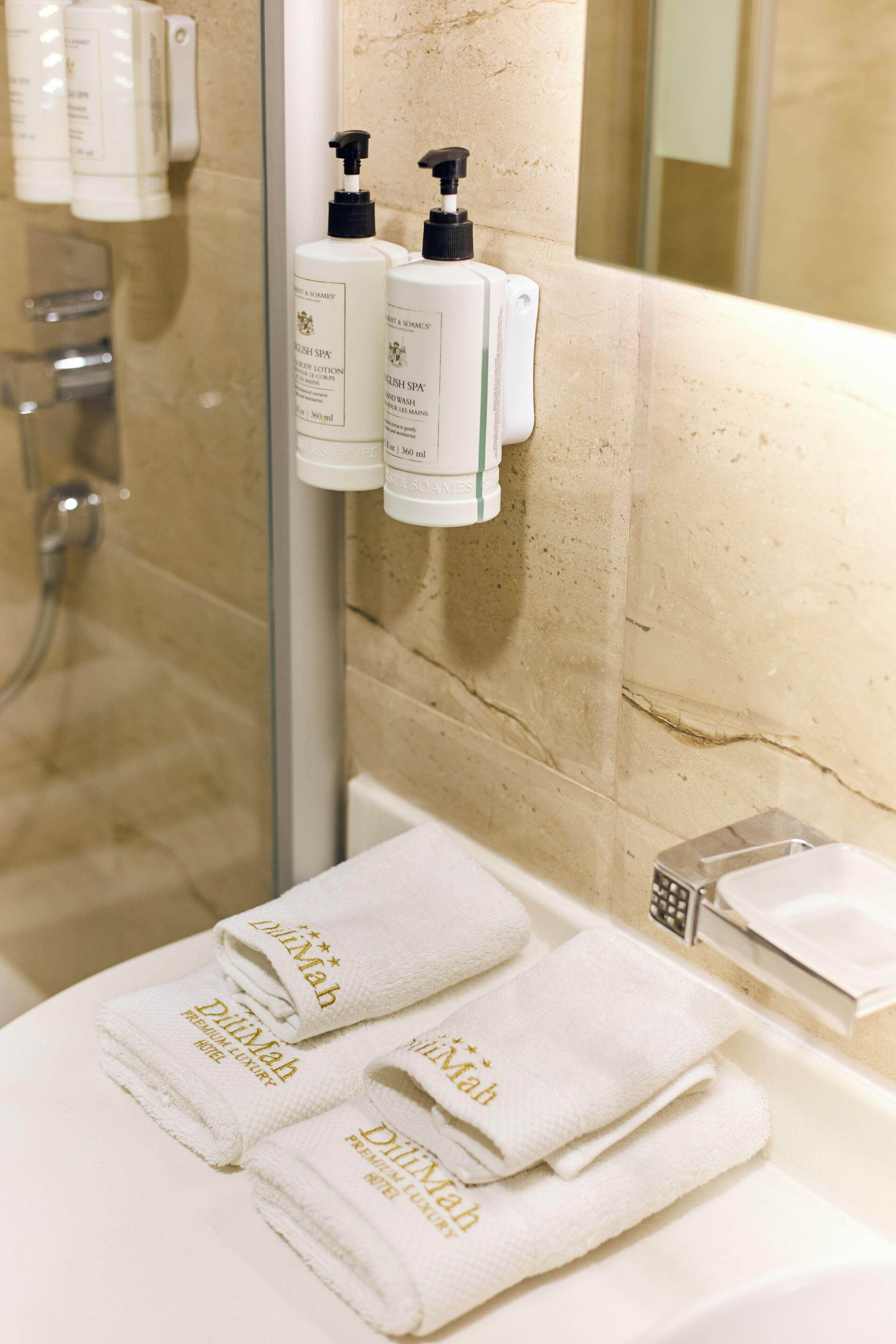 A bathroom with a glass shower enclosure, a white sink, and two bottles of body lotion.