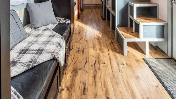 Un interior moderno y compacto con suelo de madera, un sofá, una escalera y una zona de cocina.