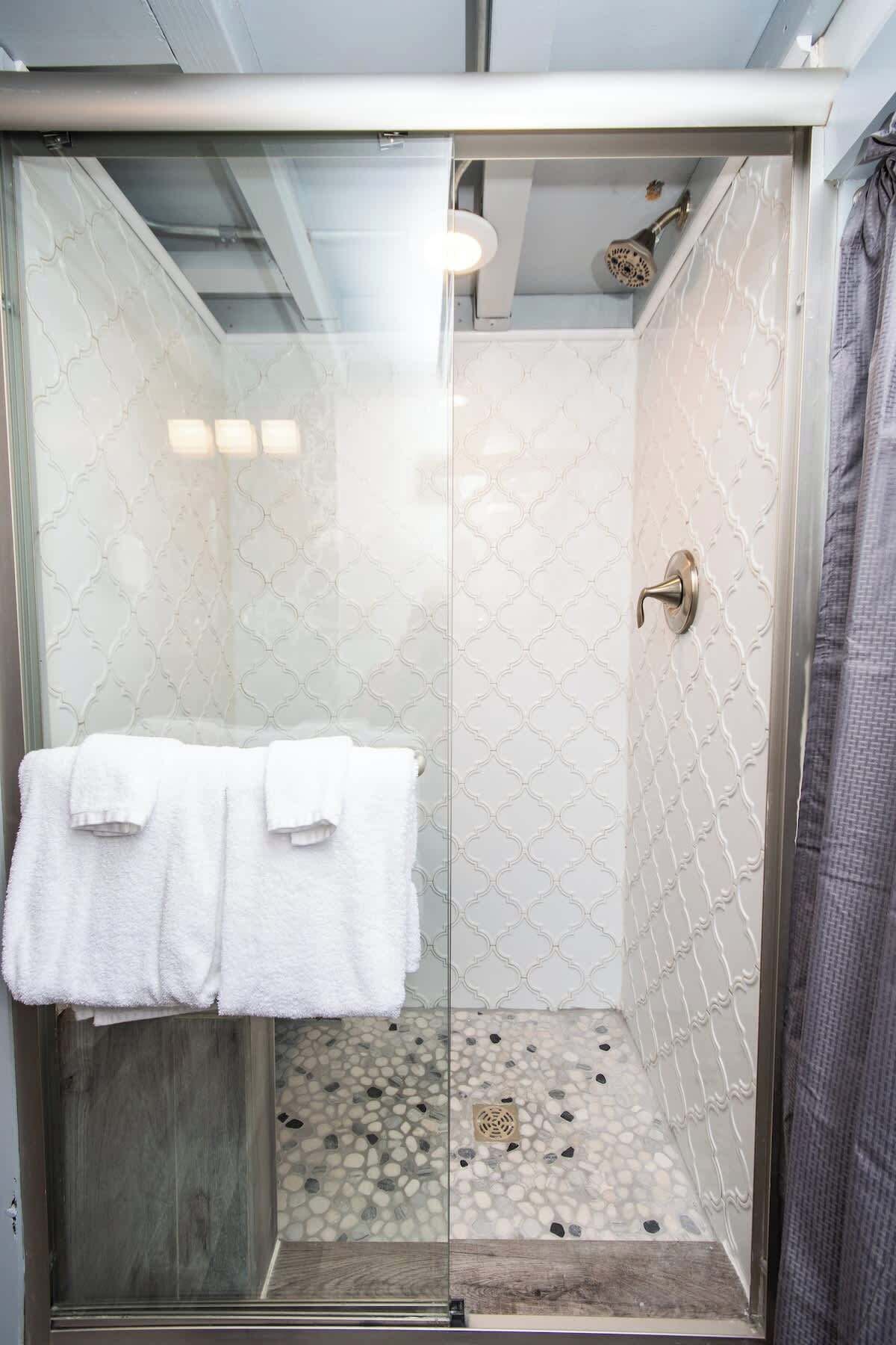 A glass-enclosed shower with a patterned tile wall, a towel rack with two towels, and a pebble-patterned floor.