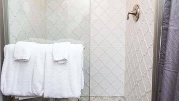 A glass-enclosed shower with a patterned tile wall, a towel rack with two towels, and a pebble-patterned floor.