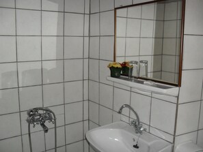 A bathroom with white tiled walls, a white sink, a mirror, and a shower.