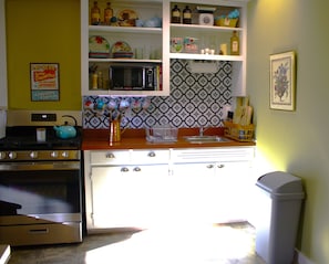 Una cocina con estufa, horno, microondas y fregadero. Hay armarios sobre la encimera y un cubo de basura a la derecha.