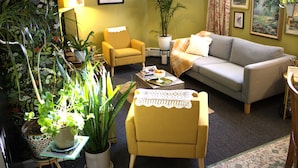 A living room with a sofa, armchair, coffee table, and various potted plants.