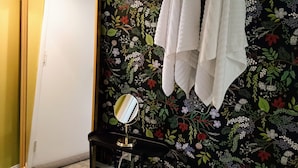 A bathroom with a floral wallpaper, a mirror, and towels hanging on the wall.