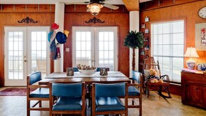 Un coin repas avec une table en bois, des chaises bleues, un ventilateur de plafond et une horloge au mur.