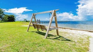 Ein Holzschaukelstuhl am Strand mit freiem Blick auf das Meer und einen entfernten Steg.