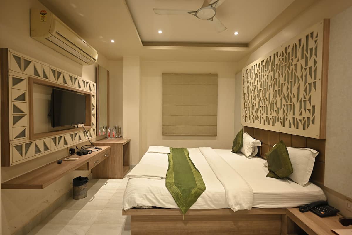 Een moderne hotelkamer met een groot bed, een flatscreen televisie bevestigd aan een houten console, een plafondventilator en een decoratief wandpaneel.