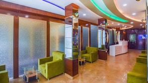 Un área de recepción de diseño moderno, con mostrador de recepción, sillas verdes y un espejo grande.