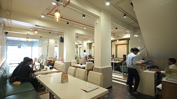 Un restaurante moderno con mesas altas, cabinas, una zona de bar y una escalera que lleva a un nivel superior.