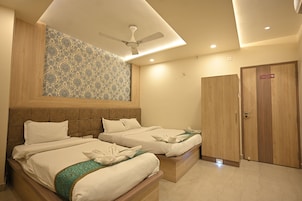 A hotel room with two beds, a ceiling fan, a wooden wardrobe, and a patterned wall.
