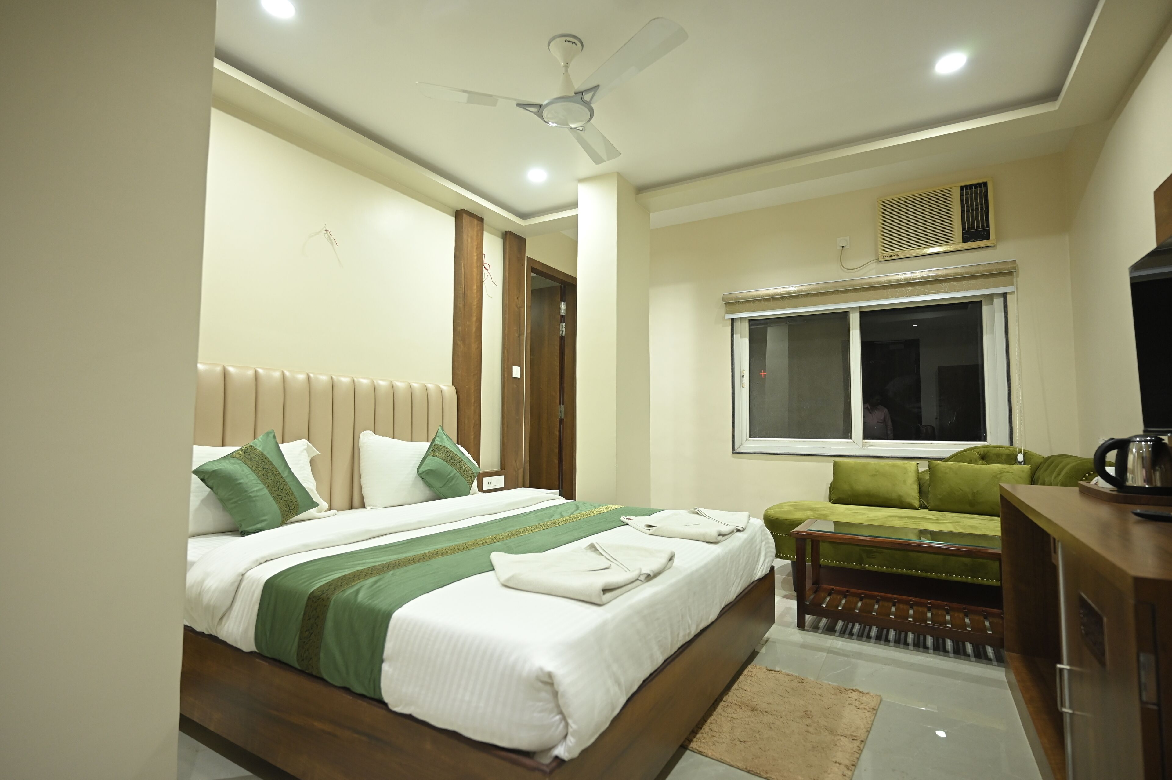 A hotel room with a bed, a green sofa, a wooden coffee table, and a ceiling fan.