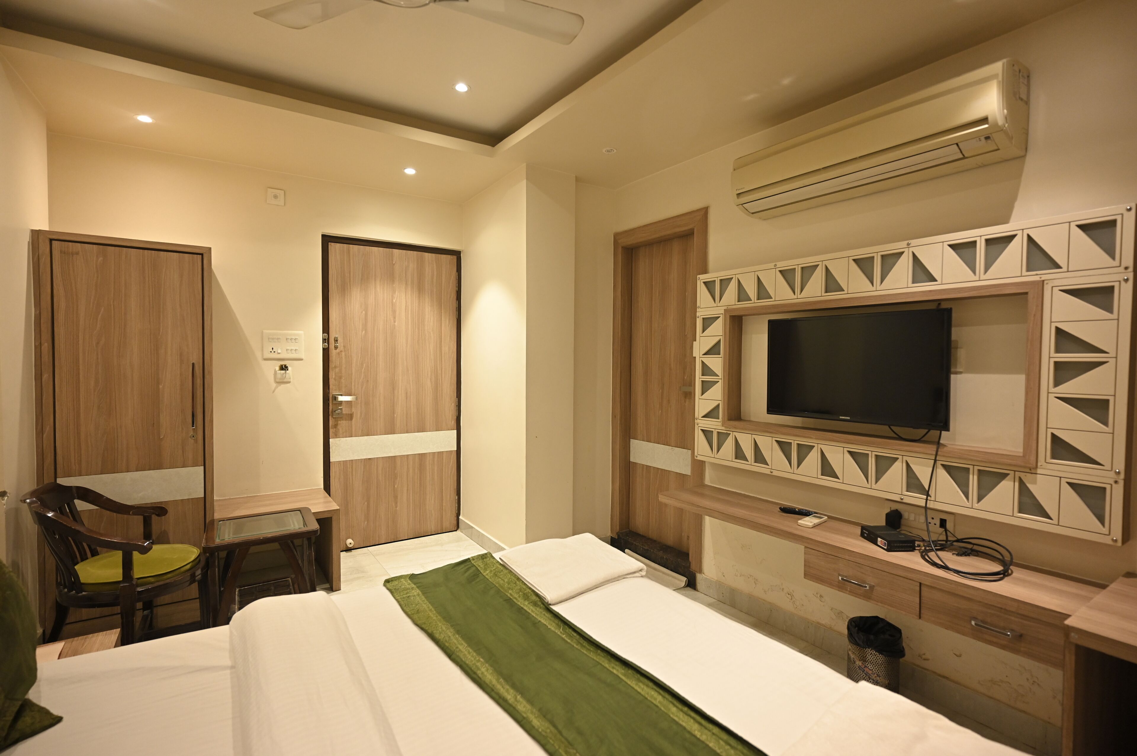 Habitación de hotel con cama, escritorio con silla, televisor y equipo de aire acondicionado.