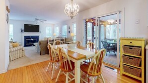 A spacious living room with a fireplace, a dining area with wooden chairs, a chandelier, and a sliding glass door leading to an outdoor area. - Free Daily Activities, Bikes,Grill, Pool&Tennis, BHChairs, 5 MINUTES from Beach! (Ocean View)