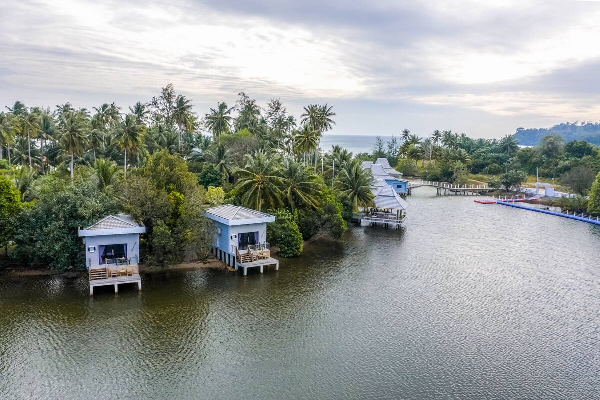 A waterway with floating structures, surrounded by dense tropical vegetation and palm trees.