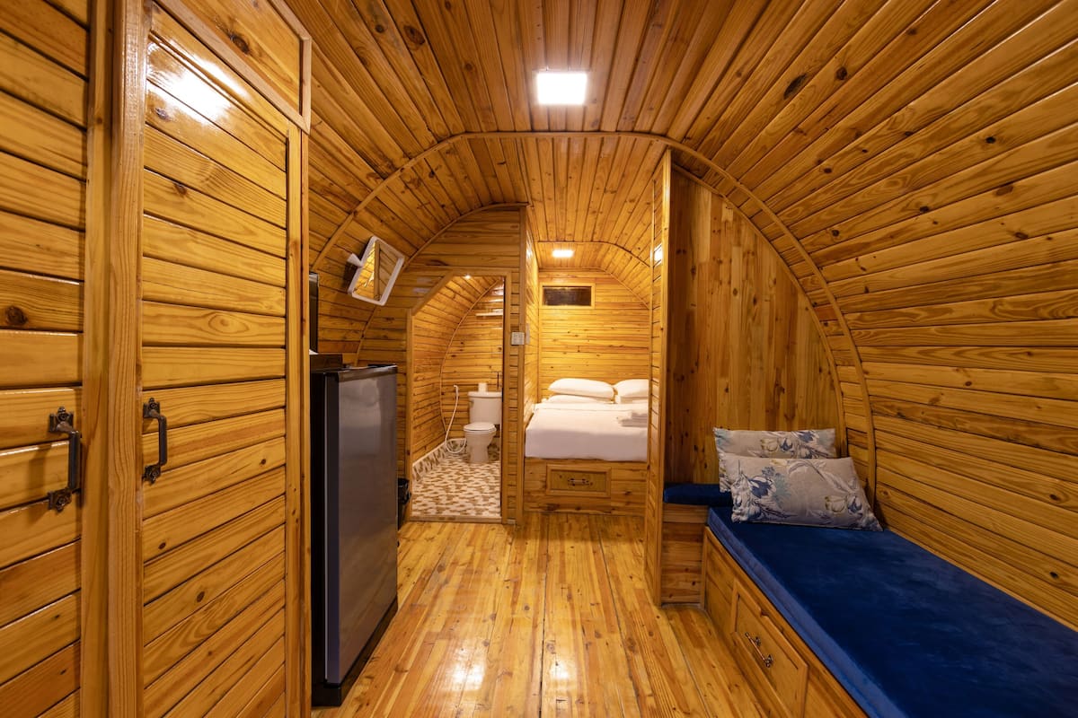 A wooden interior with a bed, a small bathroom, and a refrigerator.