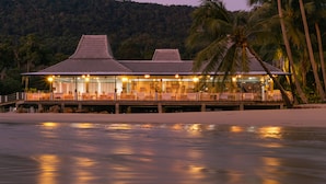 Un hotel frente a la playa con techo tradicional, asientos al aire libre y vista al océano.