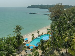 A beach resort with a swimming pool, palm trees, and a pier extending into the water.