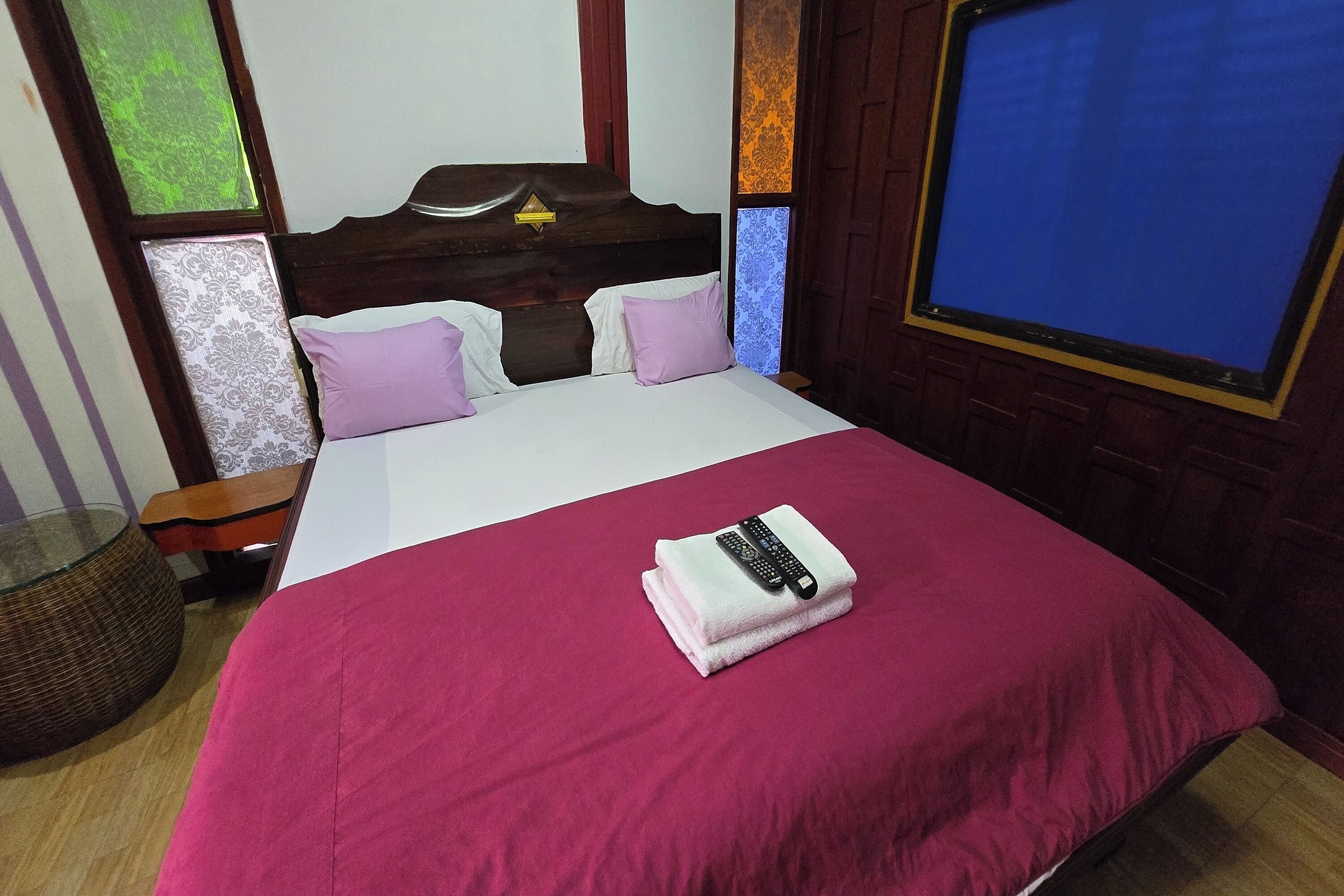 Una cama bien hecha con una colcha roja, una almohada blanca y una toalla doblada, con un control remoto encima.
