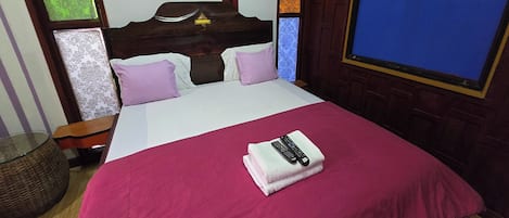 Una cama bien hecha con una colcha roja, una almohada blanca y una toalla doblada, con un control remoto encima.