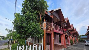 Et traditionelt hus med balkon, hvidt stakhegn og gade i baggrunden.