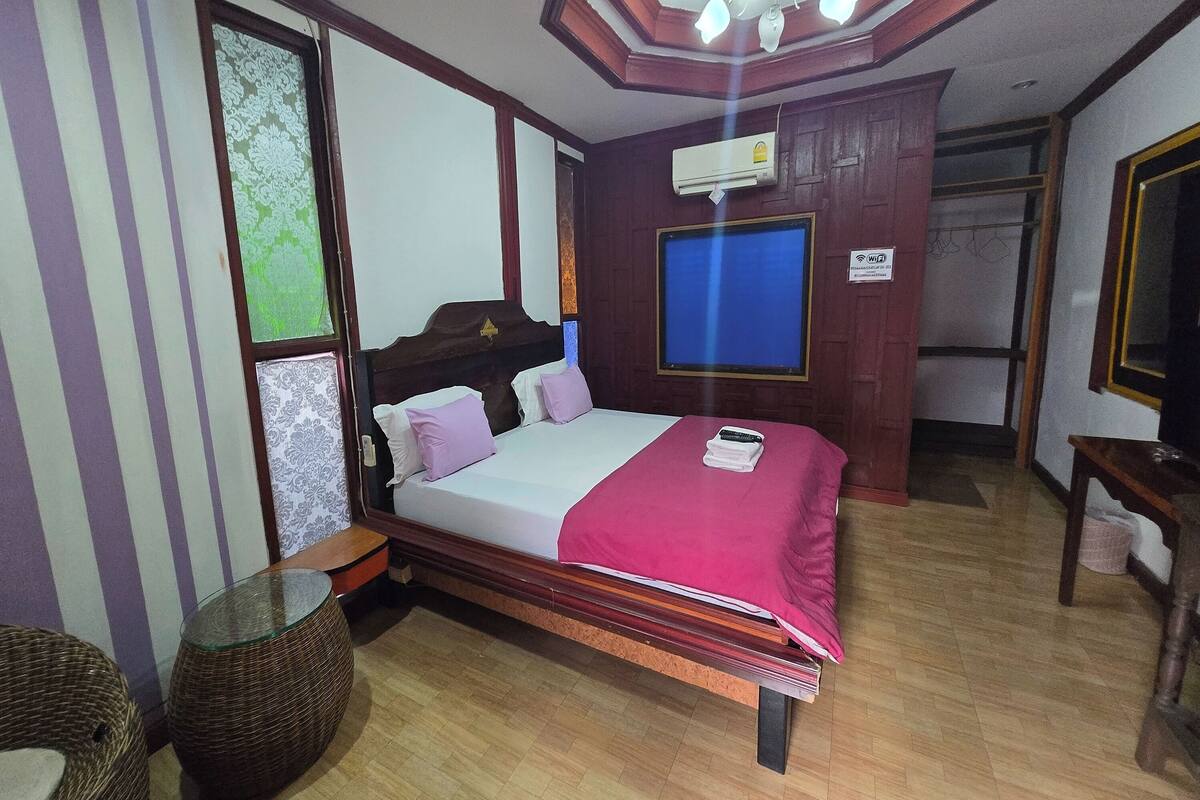 A hotel room with a wooden bed, a window with a view, a ceiling fan, and an air conditioning unit.