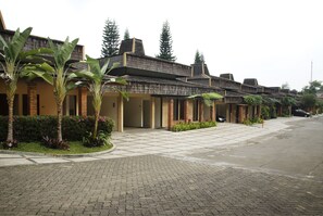 A row of traditional-style buildings with brick facades and tiled roofs, lined with palm trees and potted plants. - The Cipaku Garden Hotel (Bandung)