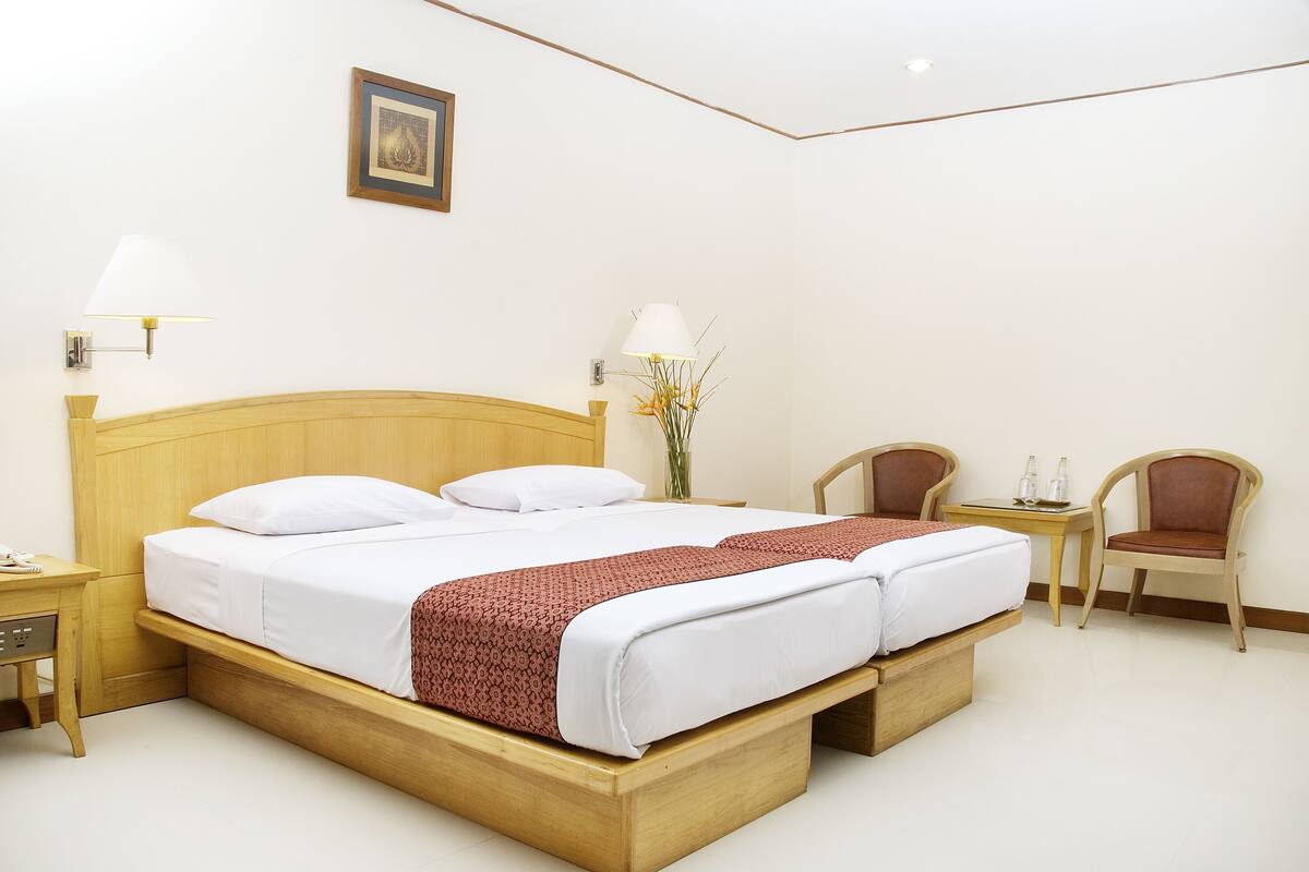 Ein Hotelzimmer mit einem hölzernen Bett, zwei Nachttischen, einem Beistelltisch, einem Sessel und einem kleinen Tisch mit zwei Flaschen.