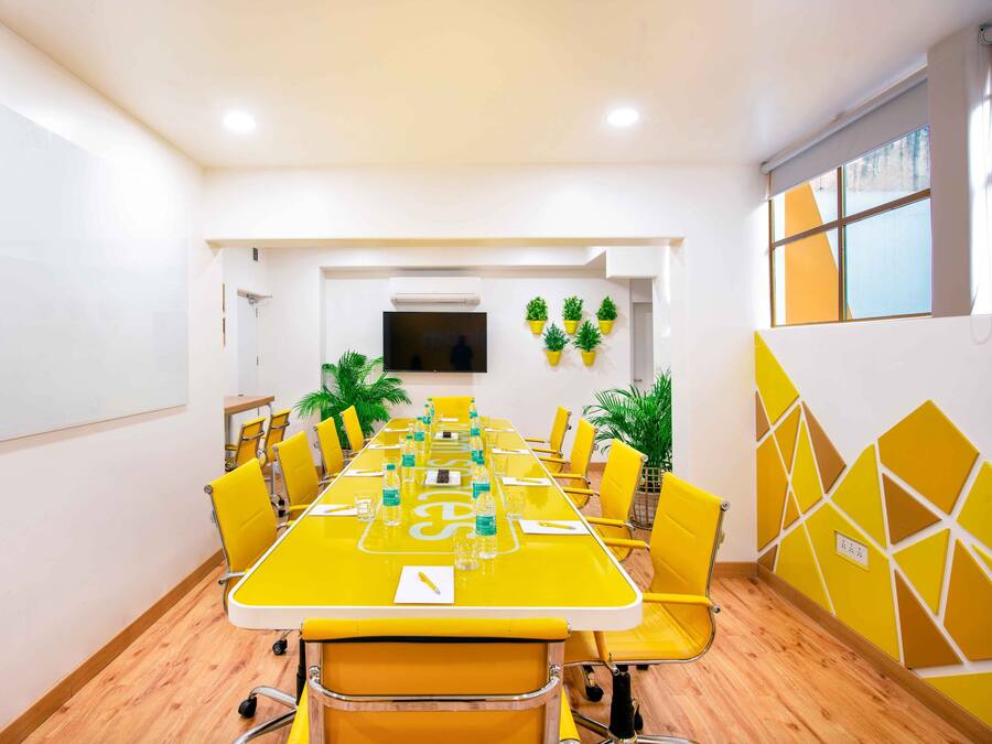 Un salón de conferencias con una larga mesa, sillas amarillas y plantas en macetas.