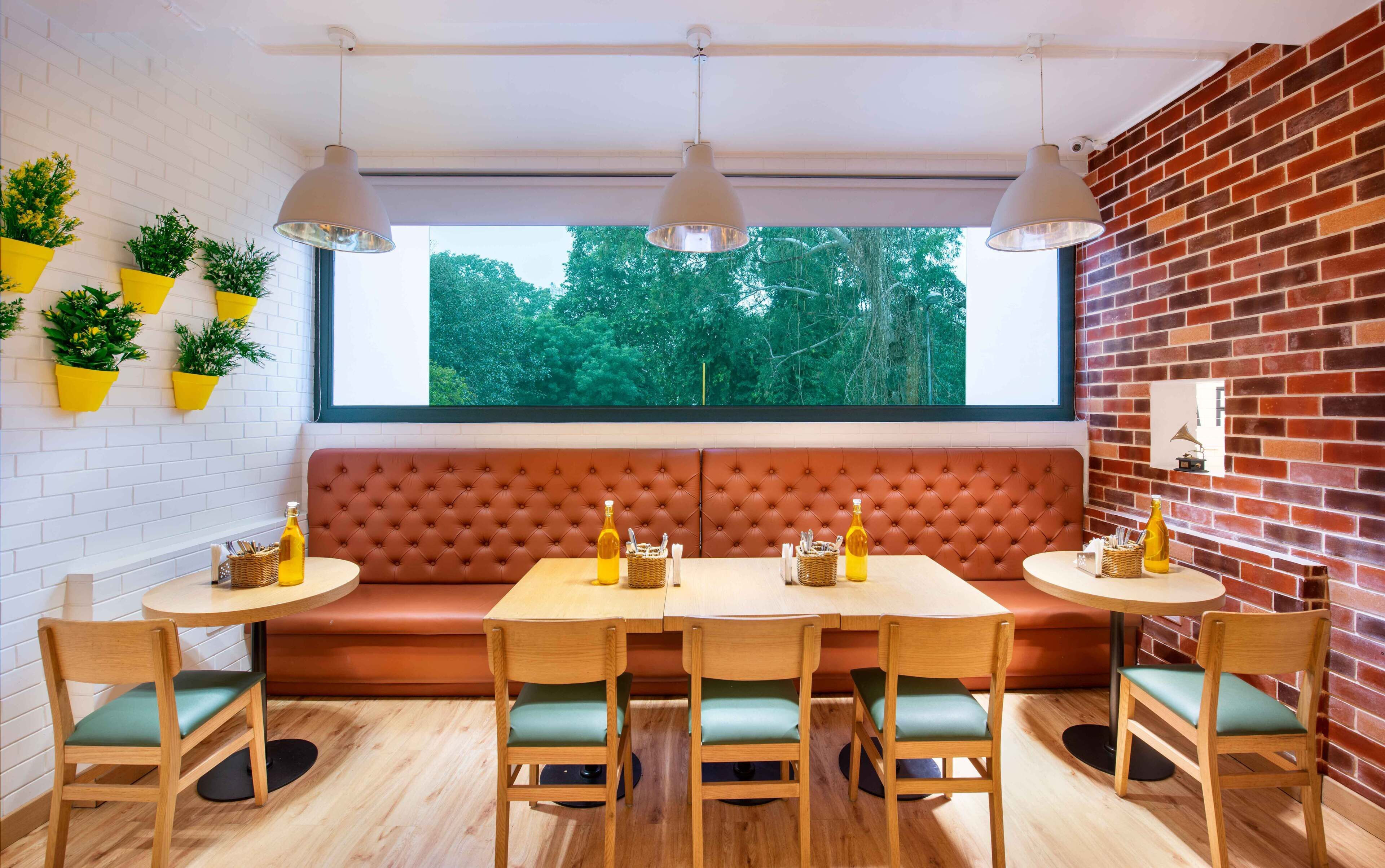Un comedor acogedor con una mesa de madera, sillas acolchadas, un banco tapizado rojo y plantas en macetas en la pared.