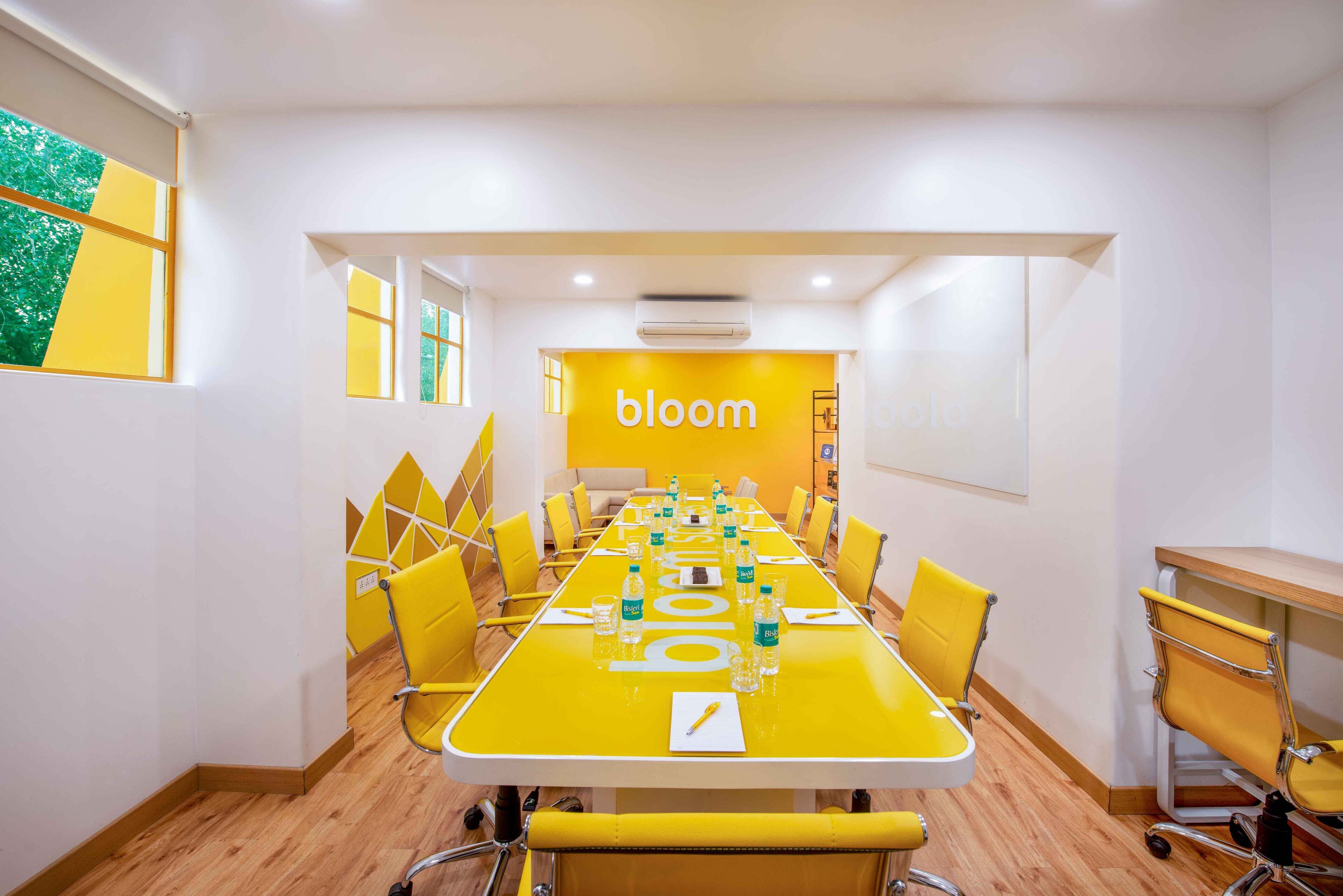 Uma sala de conferências com uma mesa comprida, cadeiras amarelas e um letreiro com a palavra 'bloom' na parede.
