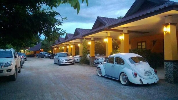 A parking area with several cars, including a vintage white car, and a building with a tiled roof and columns. - Suansiri Resort (Mae Chan)