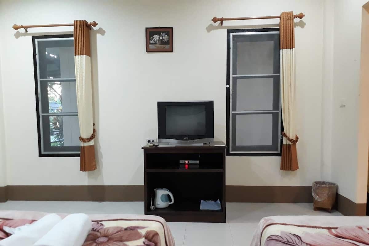 A room with two beds, a television, a small shelf with a kettle, and curtains on the windows.