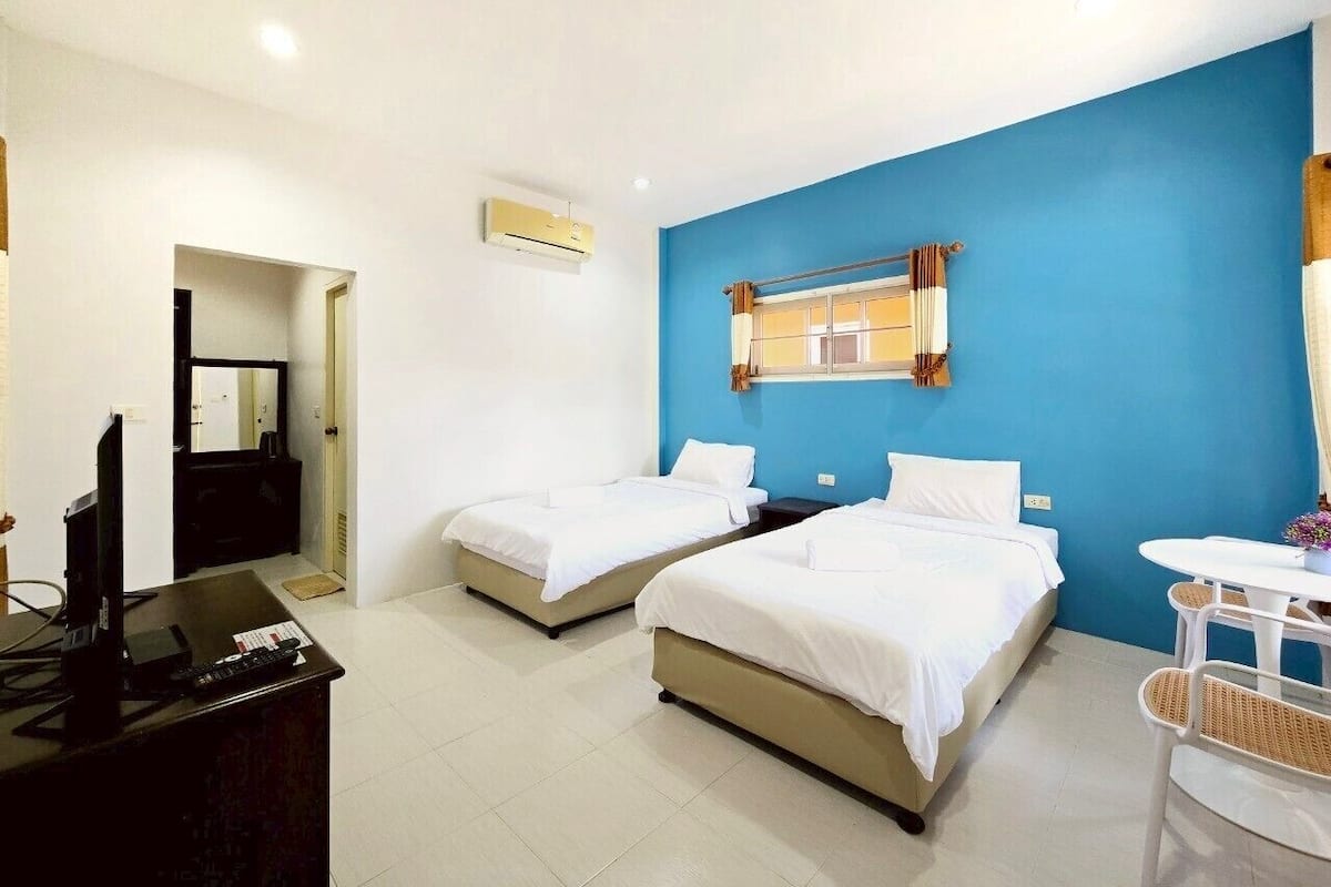 A hotel room with two single beds, a desk with a computer, a TV, and a small table with chairs.