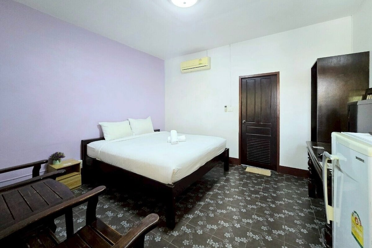 A hotel room with a single bed, a small table, a desk, and a refrigerator.
