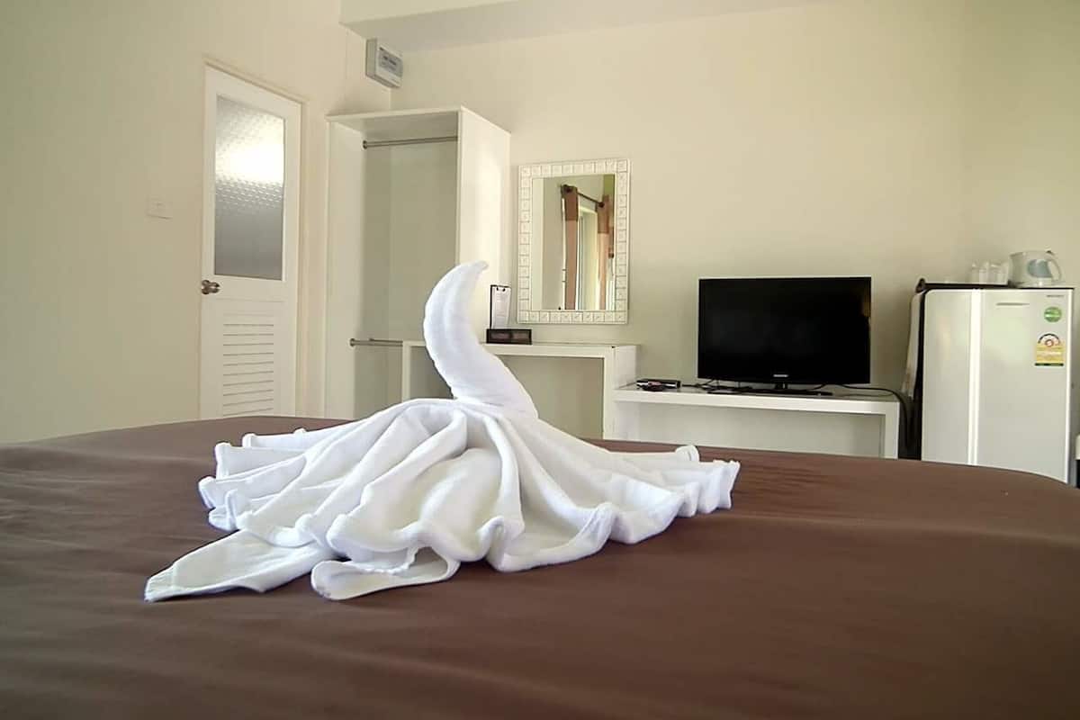 A hotel room with a bed, a television, a refrigerator, and a mirror on the wall.