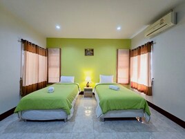 A room with two beds, a nightstand with a lamp, and an air conditioning unit on the wall.