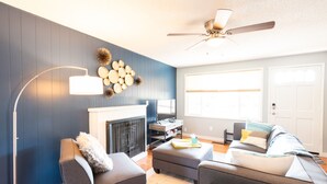 A modern living room with a fireplace, dark blue walls, and a ceiling fan. - Comfy & Bright 2BR Flat W/ Fenced Yard Near Washington Square (Tigard)