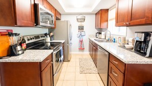 A kitchen with wooden cabinets, a refrigerator, a stove, and a coffee maker. - Comfy & Bright 2BR Flat W/ Fenced Yard Near Washington Square (Tigard)