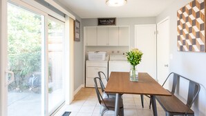 A dining area with a wooden table, metal chairs, a vase with flowers, and a laundry service sign on the wall. - Comfy & Bright 2BR Flat W/ Fenced Yard Near Washington Square (Tigard)