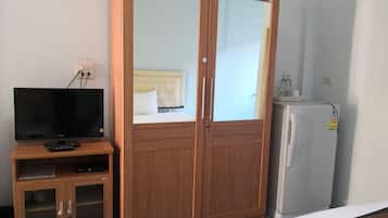 Una habitación con un armario de madera, un televisor sobre un mueble de madera y un refrigerador.