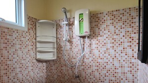 Un baño con pared de ducha en azulejos, un lavamanos pedestal blanco y un cabezal de ducha de mano.