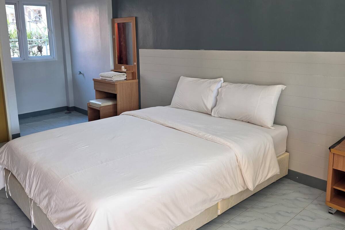 Ein Schlafzimmer mit einem großen Bett, einem Nachttisch aus Holz, einem Spiegel und einem Fenster.