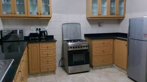 A kitchen with wooden cabinets, a gas stove, a microwave, and a refrigerator. - Samaritan Homes (Nairobi)