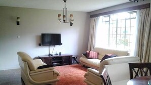 A living room with a sofa, two armchairs, a TV, a small table, and a patterned rug. - Samaritan Homes (Nairobi)