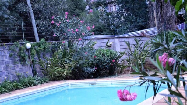 A swimming pool surrounded by lush greenery and flowering plants. - Samaritan Homes (Nairobi)